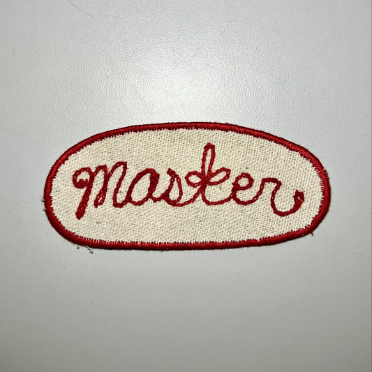 Oval patch with "Master" in red chainstitch embroidery and a red border.